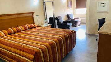 Una habitación de hotel con una cama grande, un escritorio, dos sillones, un espejo y un termostato en la pared.