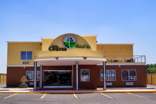 A hotel entrance with a clear sign, a covered entrance area, and a parking lot. - Los Cedros Hotel Inn Torreon (Torreón)