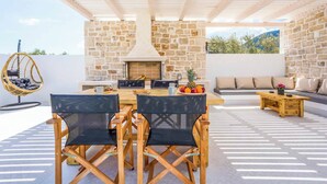 An outdoor patio with a stone wall, a wooden table with chairs, a hanging chair, and a seating area with cushions.