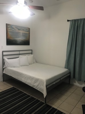 A single bed with a headboard, a painting on the wall, and a ceiling fan.