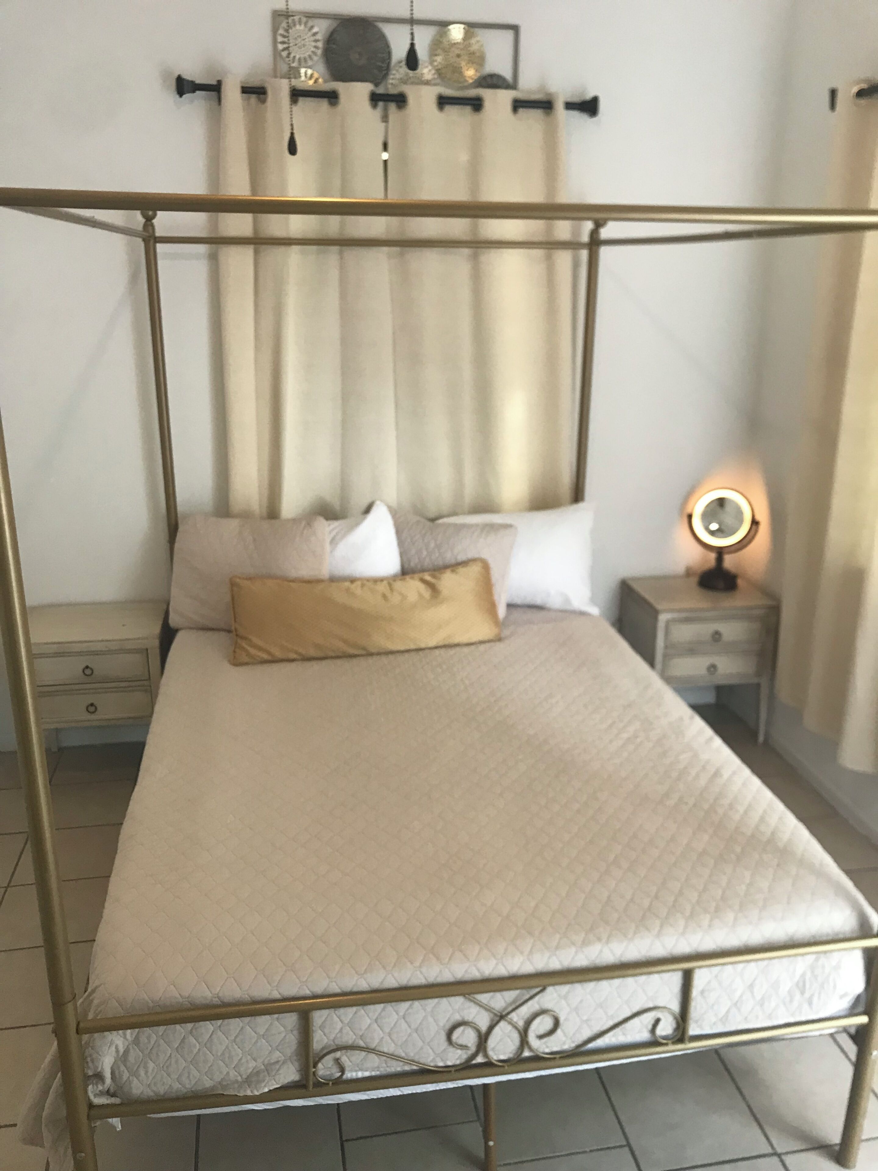A four-poster bed with a quilted mattress, a bedside table with a lamp, and a curtain rod with a single curtain.