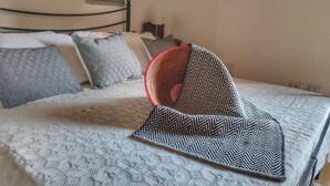 A bed with a patterned bedspread and several pillows, including a red woven one. - "Loft delle Concerie: History and Comfort in the Heart of Bosa" (Bosa)
