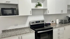 Une cuisine moderne avec des meubles blancs, un micro-ondes noir, une cuisinière en acier inoxydable et un plan de travail en granit.