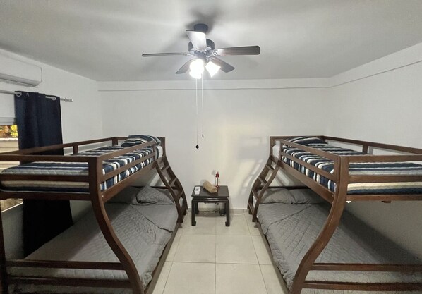 Une chambre de dortoir équipée de deux lits superposés, d’un ventilateur de plafond, d’une petite table et d’un radiateur fixé au mur.