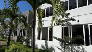 Un bâtiment moderne doté de nombreuses fenêtres et d’un jardin bien entretenu, agrémenté de palmiers.