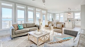 A spacious living room with a large window, a ceiling fan, and a view of the city. - Luxurious 7BR Beach Home w/ Ocean Views, Pool, Hot tub, and Elevator (North Topsail Beach)