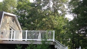 Eine Holzterrasse mit weißer Reling, umgeben von dichtem Grünwerk.