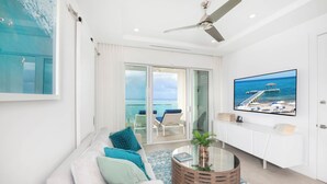 A modern living room with a white sofa, a round coffee table, and a television on a white cabinet. - Rum Point Resort 207 by Grand Cayman Villas (Grand Cayman)