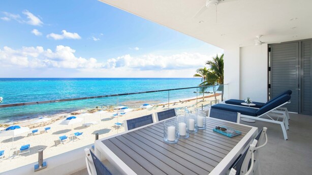 A balcony with a view of the beach and ocean, a table with candles, and lounge chairs. - Rum Point Resort 207 by Grand Cayman Villas (Grand Cayman)