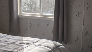 A bedroom with a bed, a window with curtains, and floral wallpaper. - Remote cabin - quick access to all the U.P. has to offer. (Germfask)
