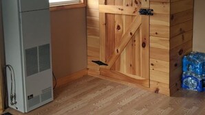 A room with a large wooden door, a white air conditioning unit, and a window with a curtain. - Remote cabin - quick access to all the U.P. has to offer. (Germfask)