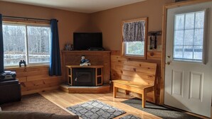 A cozy cabin interior with a fireplace, wooden furniture, and large windows offering a view of a snowy landscape. - Remote cabin - quick access to all the U.P. has to offer. (Germfask)