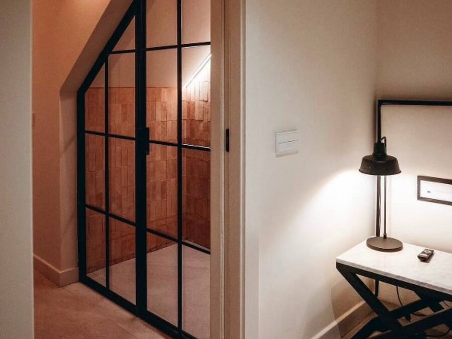 Una habitación con puerta corredera que da a un interior de madera, una mesa con lámpara y un interruptor de luz en la pared.