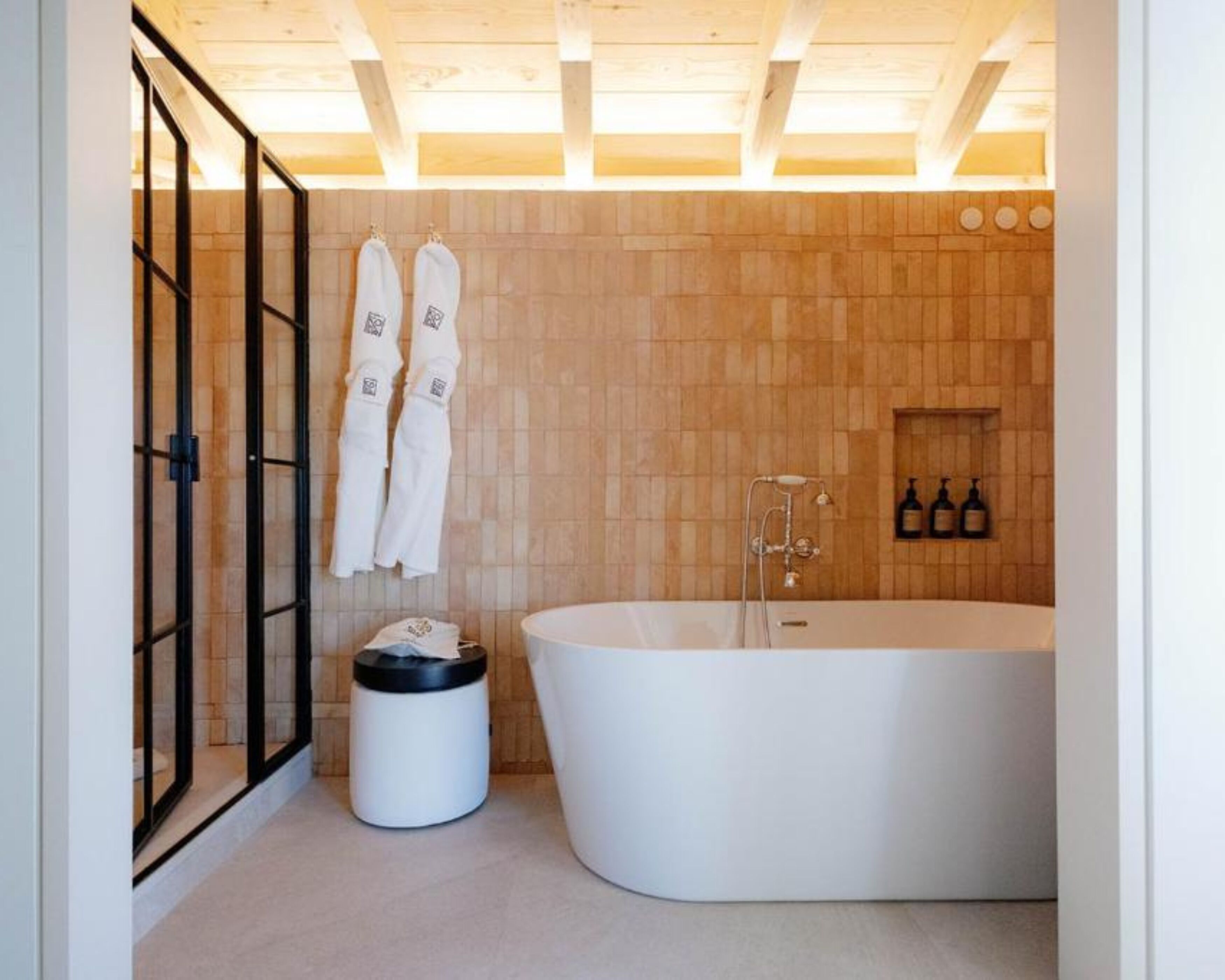 A modern bathroom with a freestanding bathtub, wooden wall tiles, and a towel rack with towels.