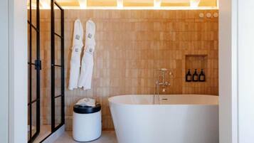 A modern bathroom with a freestanding bathtub, wooden wall tiles, and a towel rack with towels.
