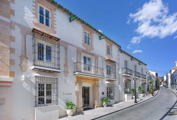 A row of white buildings with balconies, a clear blue sky, and a street in the background.