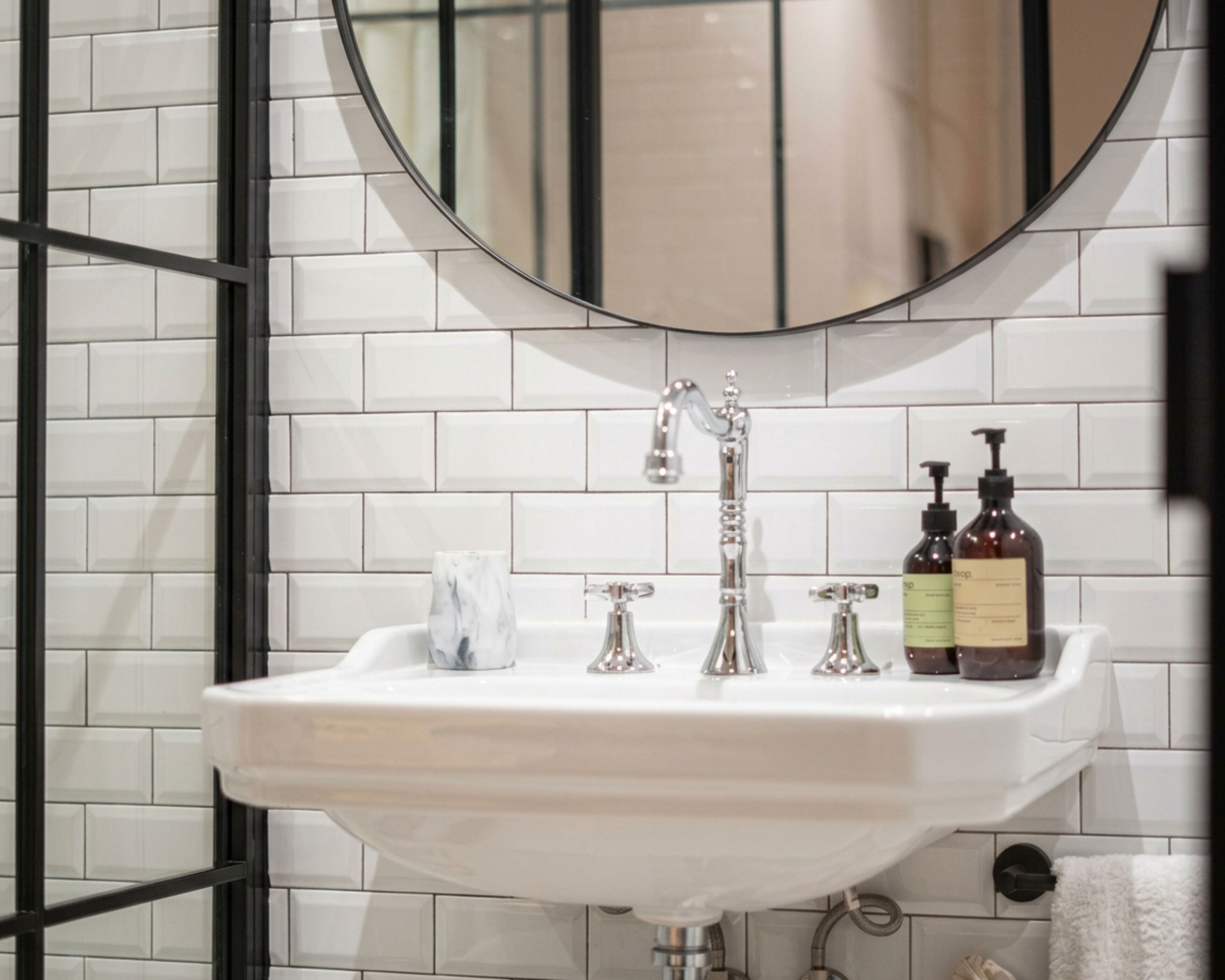 Un baño con un lavamanos blanco, dos grifos, un espejo y dos botellas de jabón.