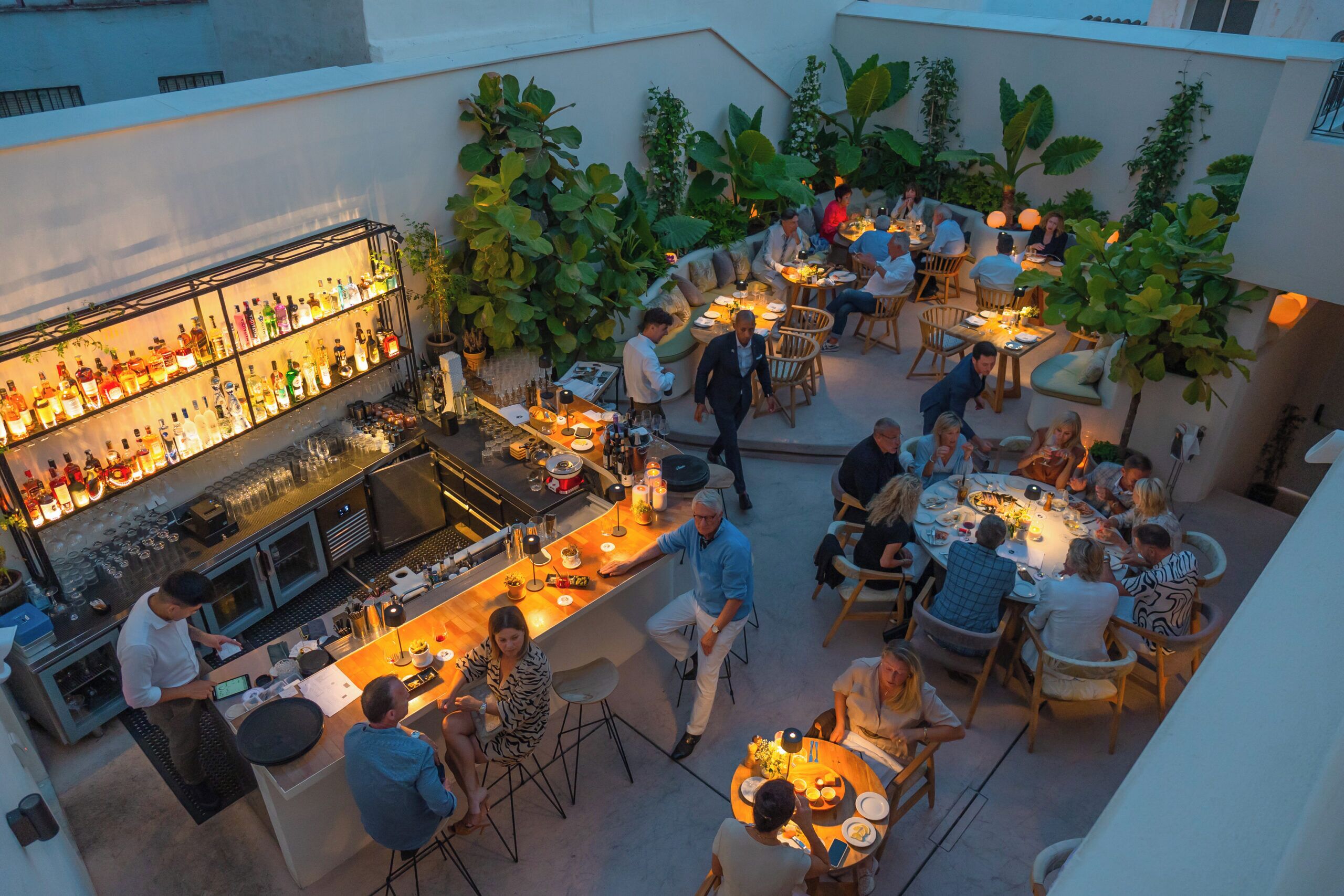 An outdoor dining area with multiple tables and chairs, surrounded by lush greenery.
