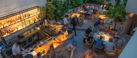An outdoor dining area with multiple tables and chairs, surrounded by lush greenery.