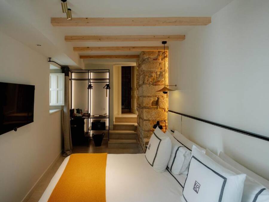 Un dormitorio con cama, televisión, pared de piedra y una zona de cocina.