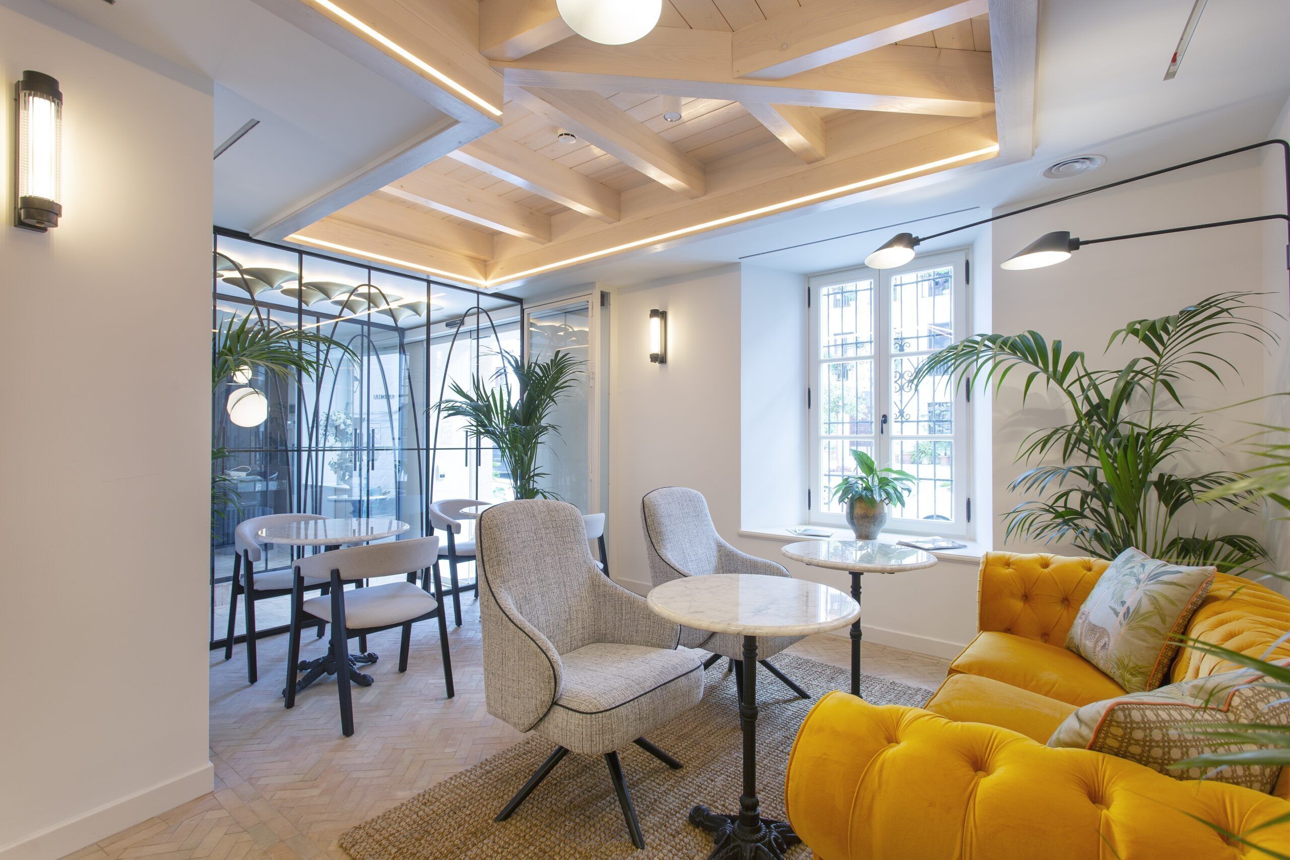 Un interior moderno con un sofá amarillo, un comedor de cristal y un techo de madera.