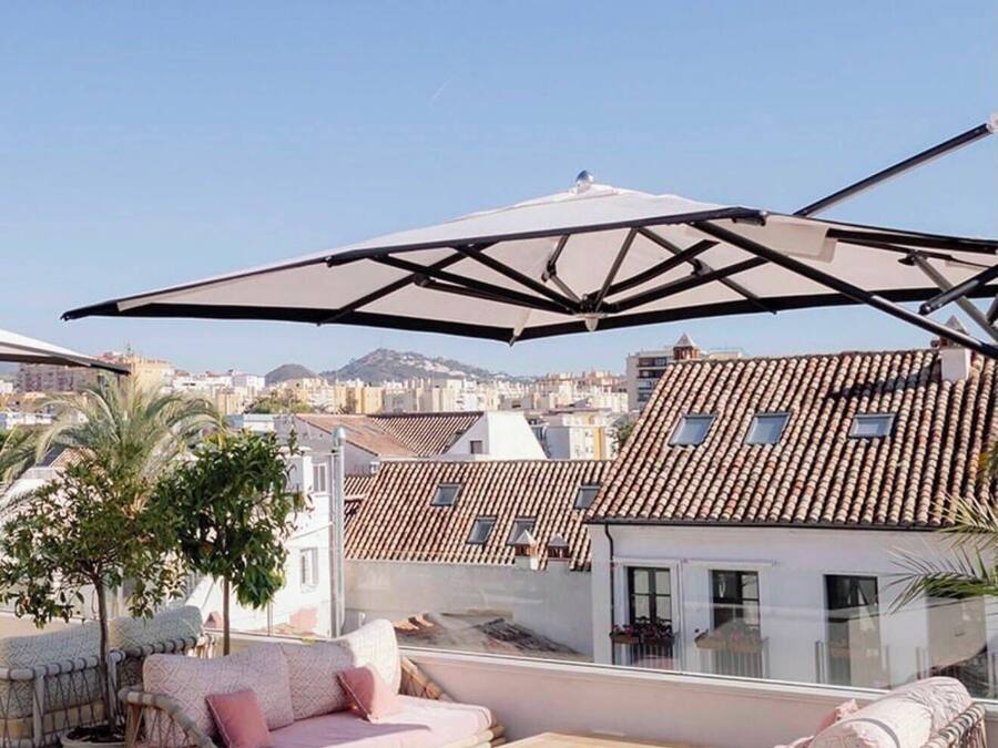 Terraço no telhado com mobiliário de exterior, um grande guarda-sol e vista para a paisagem urbana.