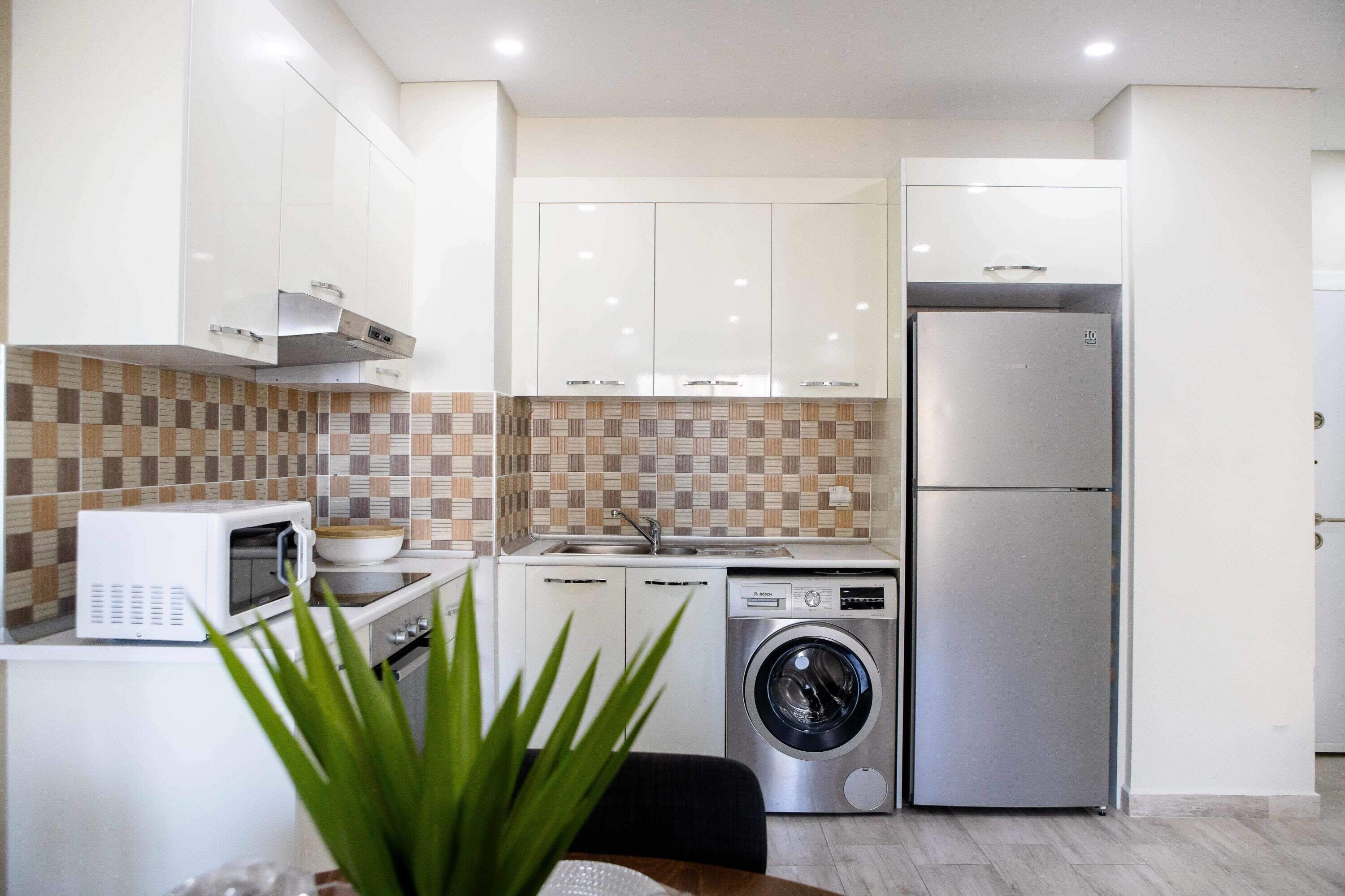 A compact kitchen with white cabinets, a microwave, a washing machine, and a refrigerator.