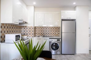 A compact kitchen with white cabinets, a microwave, a washing machine, and a refrigerator. - Maison Moz - Polana Plaza VII (Maputo)