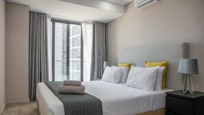 A modern hotel room with a large bed, a bedside table, and a window with curtains. - Maison Moz - Polana Plaza IV (Maputo)