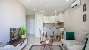 A modern living room with a sofa, TV, and dining area. - Maison Moz - Polana Plaza IV (Maputo)