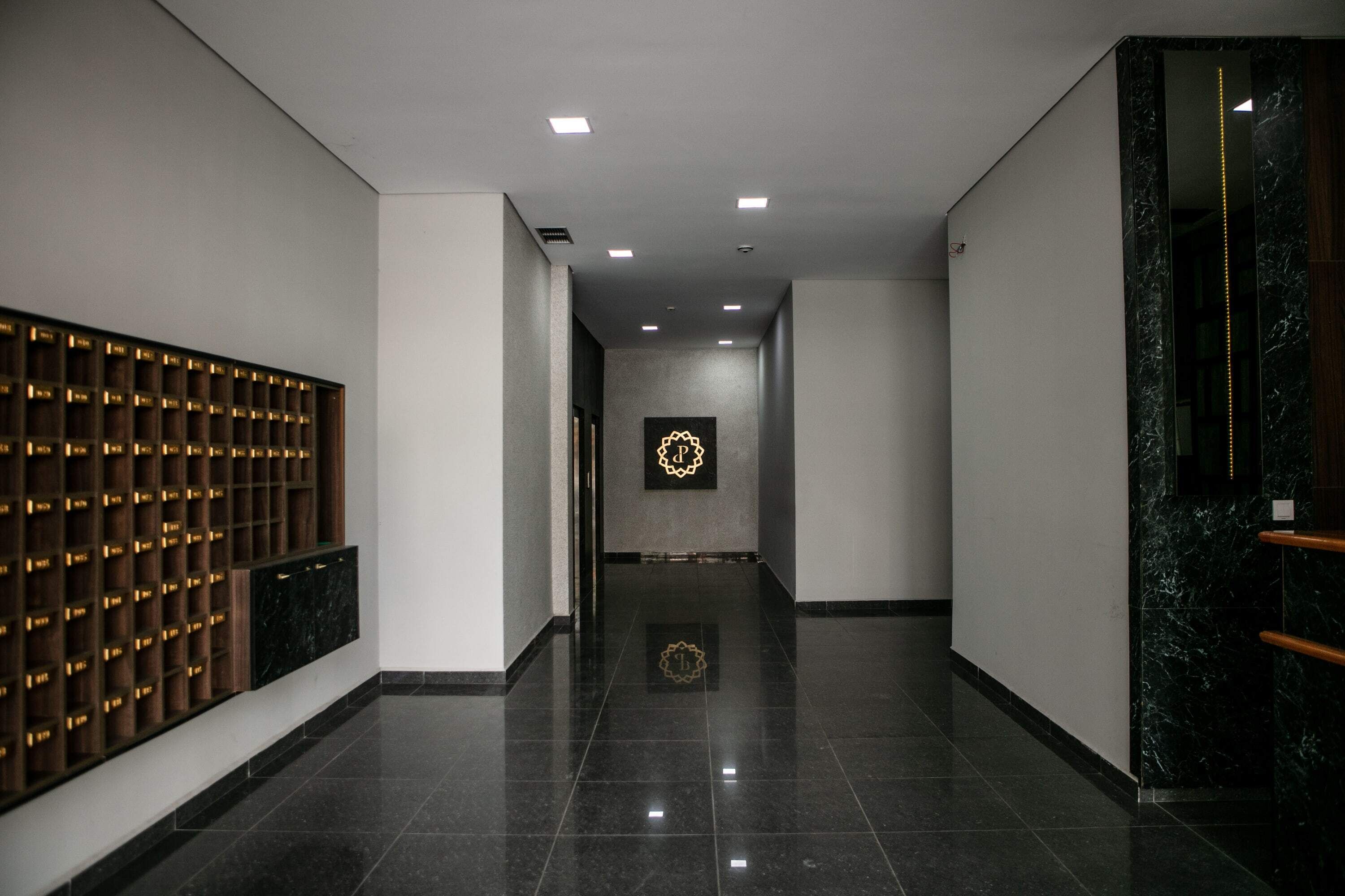 A modern hotel corridor with a reflective floor, a wooden panel wall with illuminated compartments, and a marble wall with a vertical light strip.
