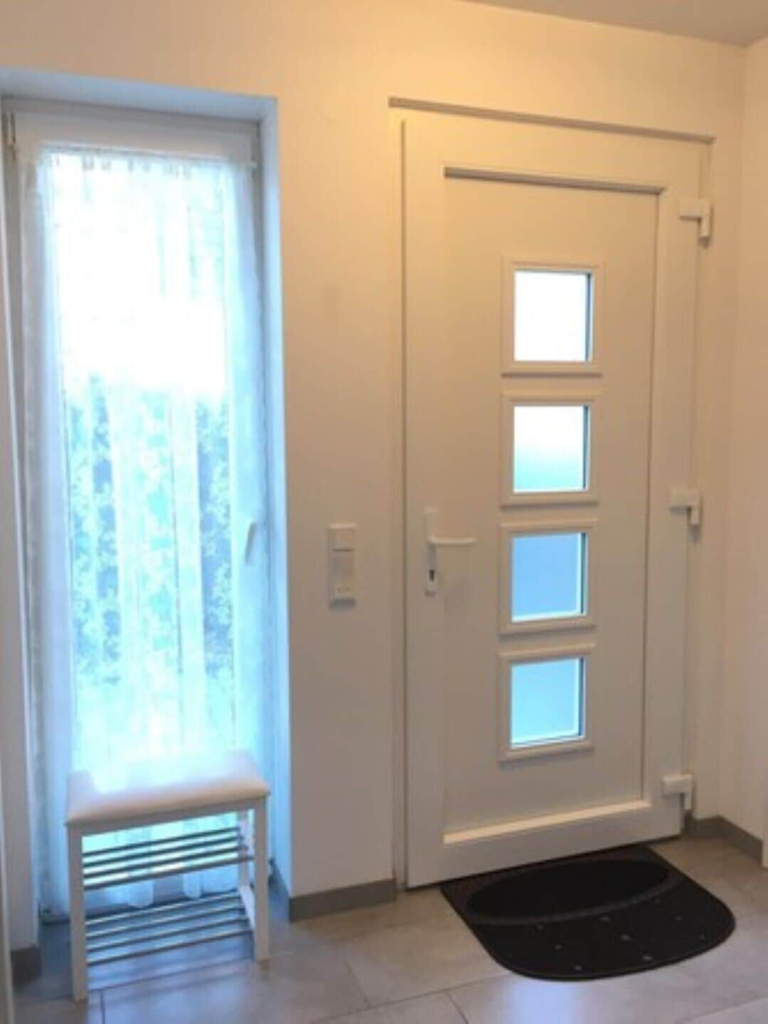 Une porte avec une fenêtre, un banc et un paillasson noir.