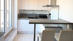 A compact kitchen with white cabinets, a black countertop, and a window providing natural light. - Vacation apartment Nara (Esens)