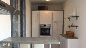 A compact kitchen with white cabinets, a built-in oven, and a small dining area with a grey table and two chairs. - Vacation apartment Nara (Esens)