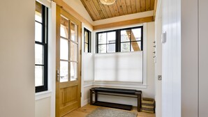 Ein Zimmer mit Holzboden, einer Bank, einer Tür und großen Fenstern mit Jalousien.