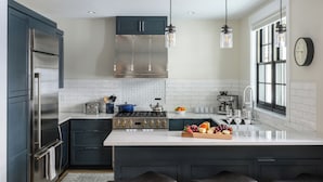 Eine moderne Küche mit einem Edelstahlkühlschrank, einem Einbauherd und einer großen Kochinsel mit Obstschale und Weingläsern.