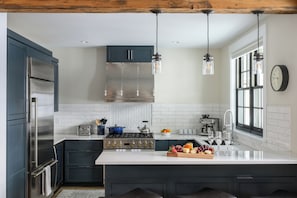 A modern kitchen with a stainless steel refrigerator, a built-in stove, and a large island with a fruit bowl and wine glasses. - Mariposa at Academy Place (Crested Butte)