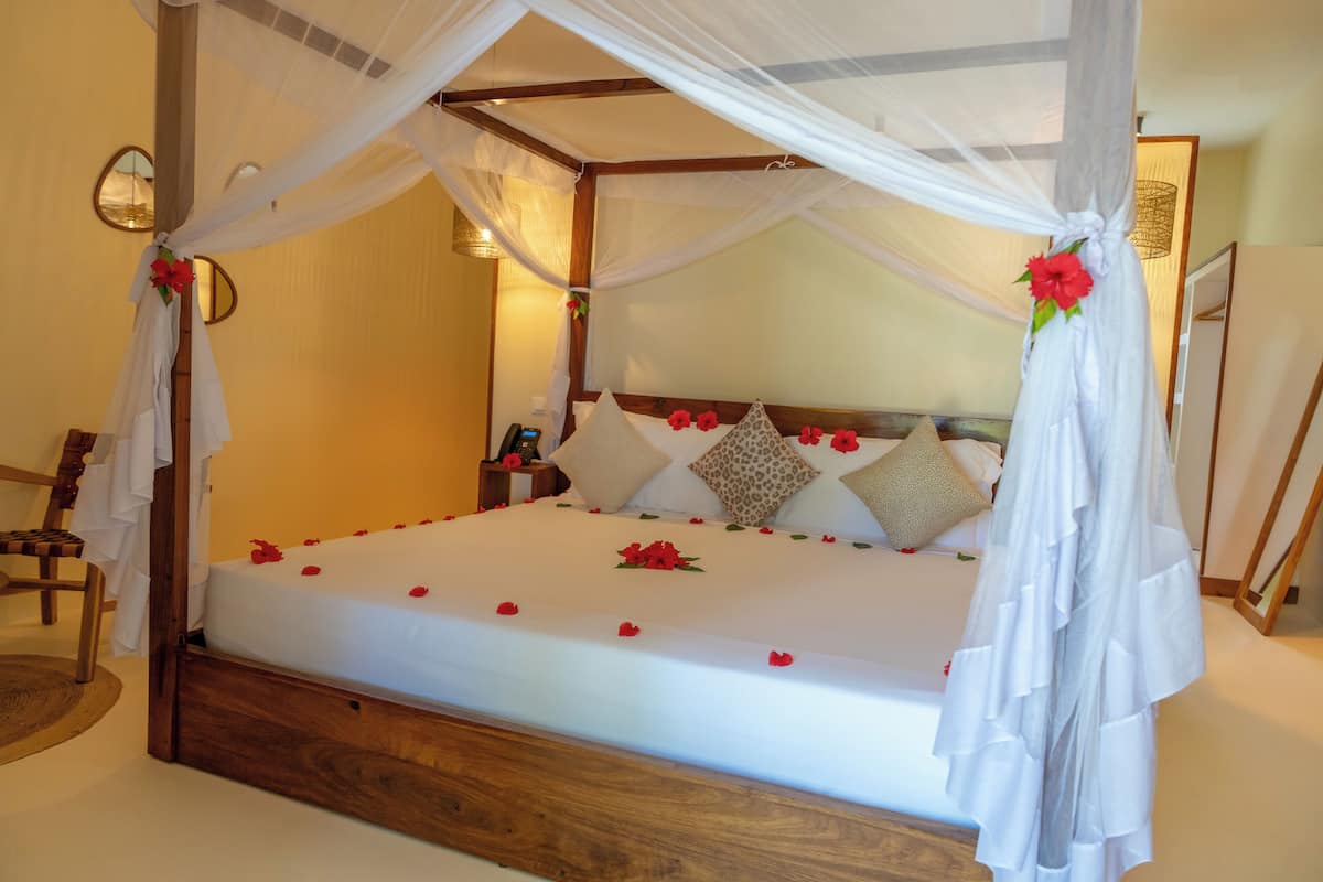 Una cama con dosel, ropa blanca y pétalos de rosa roja.