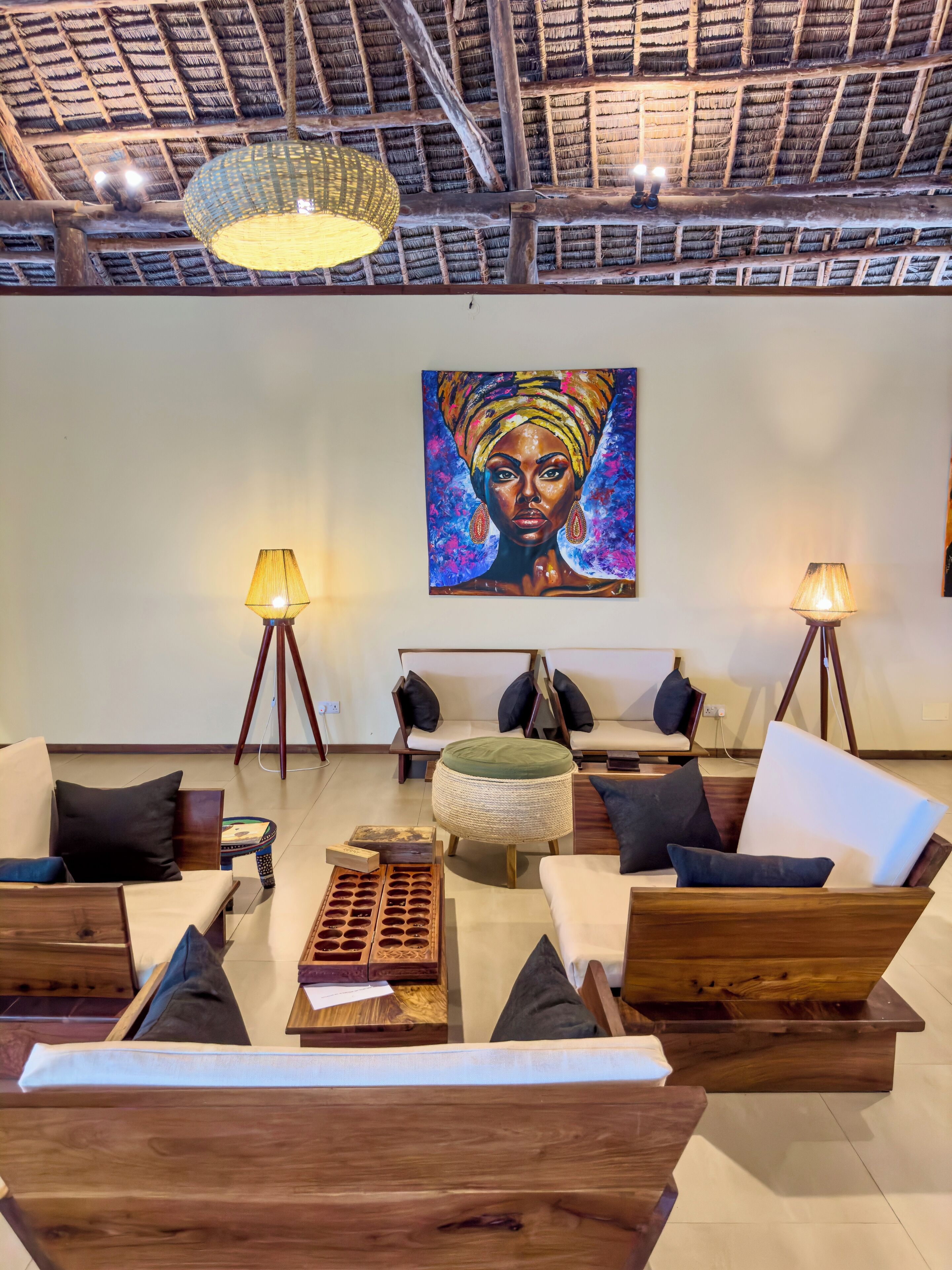 A modern living room with wooden furniture, a large painting on the wall, and two floor lamps.