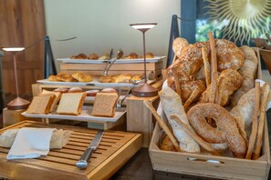 A buffet with various breads and pastries, including croissants and bagels, arranged on wooden boards and trays. - Alma Boutique Hotel (Jambiani)
