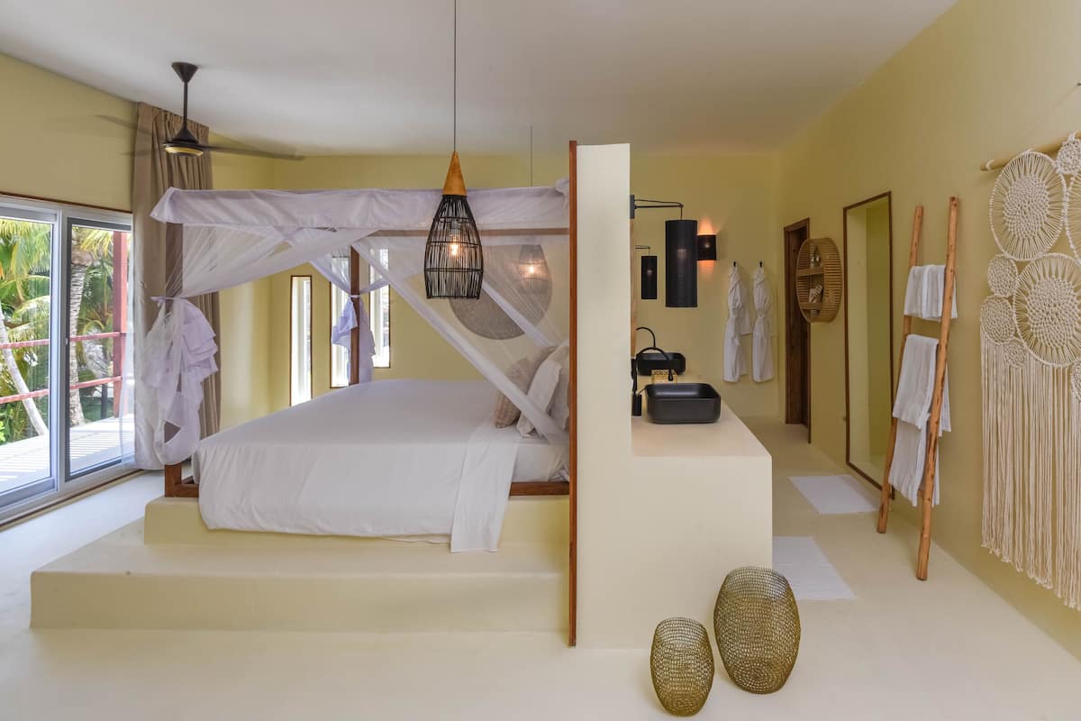Un dormitorio con cama con dosel, lámparas de noche, tocador con espejo y decoración de macramé en la pared.
