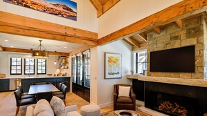 Amplia sala de estar con chimenea de piedra, televisor grande montado en la pared y un rincón de descanso acogedor con un sofá y una butaca.