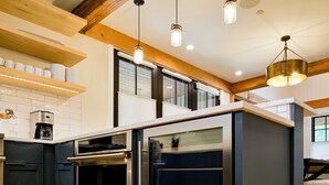A modern kitchen with dark cabinets, stainless steel appliances, wooden beams, and pendant lighting. - Academy Place | Paintbrush (Crested Butte)