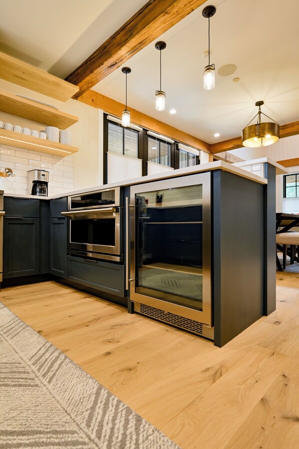 Una cocina moderna con armarios oscuros, electrodomésticos de acero inoxidable, vigas de madera e iluminación colgante.