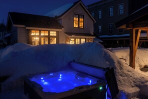 A snow-covered backyard with a hot tub illuminated by blue lights.