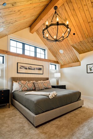 A bedroom with a large bed, a chandelier, and a framed picture on the wall.