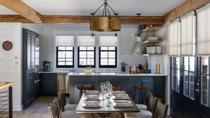 A modern kitchen with a central island, wooden beams, and a dining area with a table set for six. - Academy Place | Paintbrush (Crested Butte)