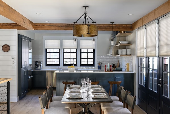 A modern kitchen with a central island, wooden beams, and a dining area with a table set for six.