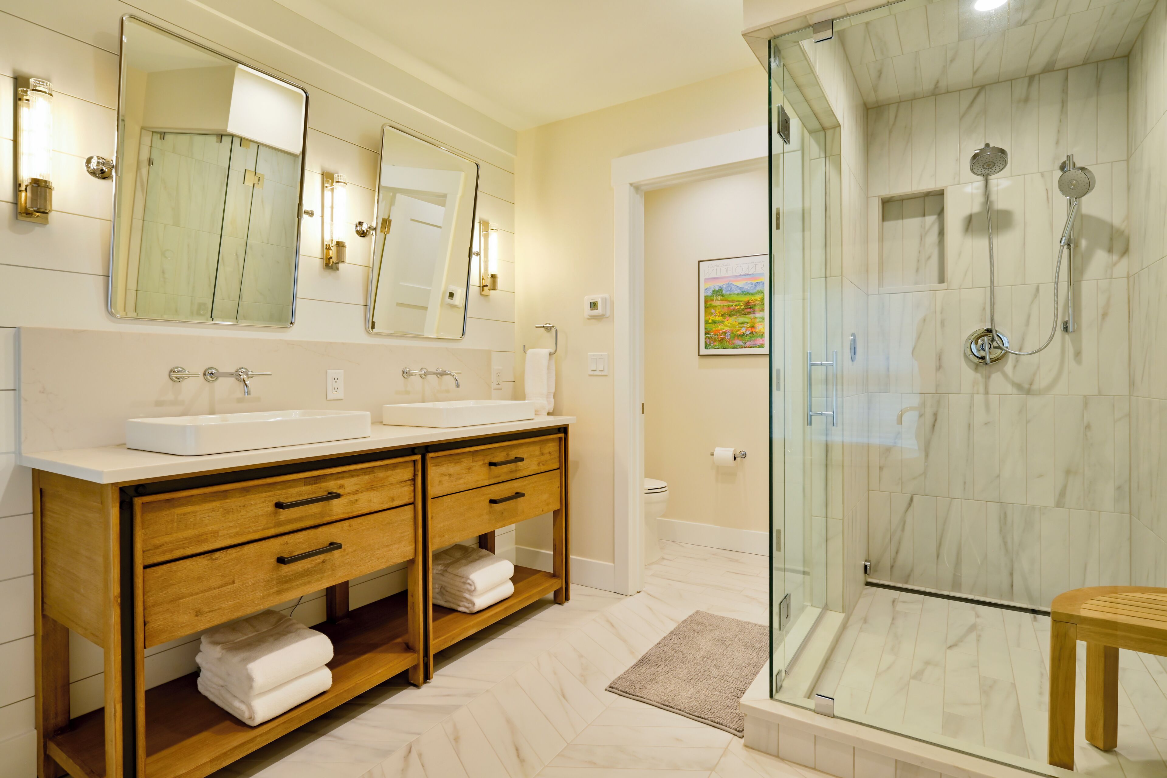 A bathroom with a glass-enclosed shower, a double sink vanity, and a wooden cabinet.