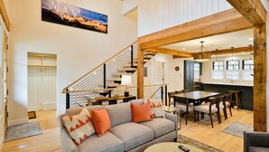 A spacious living area with a gray sofa, wooden dining table, and a staircase leading to upper floors. - Academy Place | Paintbrush (Crested Butte)